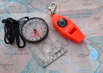 Zdjęcie przedstawia mapę, kompas i pomarańczowy gwizdek sygnałowy.