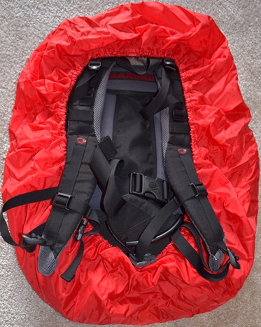 Plecak trekkingowy Mammut, w kolorze beżowo-niebieskim. Na tyle widoczny pas biodrowy i czerwony pokrowiec przeciwdeszczowy.