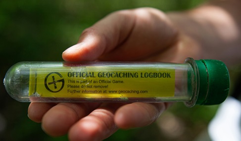 Zdjęcie przedstawia oficjalny log book gry Geocaching. Szklana lub plastikowa tubka z kartkami papieru w środku.