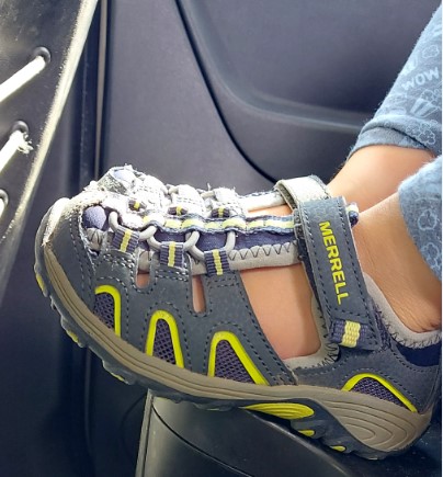 Stopy dziecka obute w sandały trekkingowe marki Merell, w kolorze niebiesko żółtym