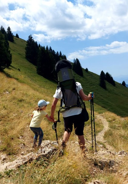 Mama idzie w górską ścieżką latem z czteroletnim dzieckiem. Na plecach ma nosidełko turystyczne