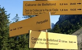 Słup informacyjny w kolorze żółtym, na rozstajach ścieżek w Alpach informujący jak daleko każda ze ścieżek prowadzi.